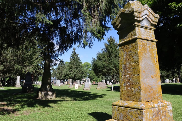 A stone monument is covered with lichen on cemetery grounds.