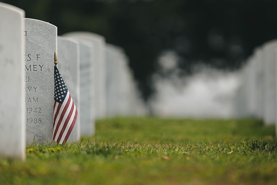 An American flag placed in front of a veteran's tombstone at a military cemetery.